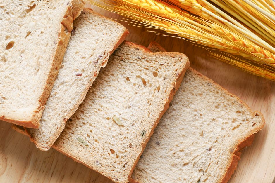 Close-up of sliced whole grain bread on a wooden surface with wheat ears.